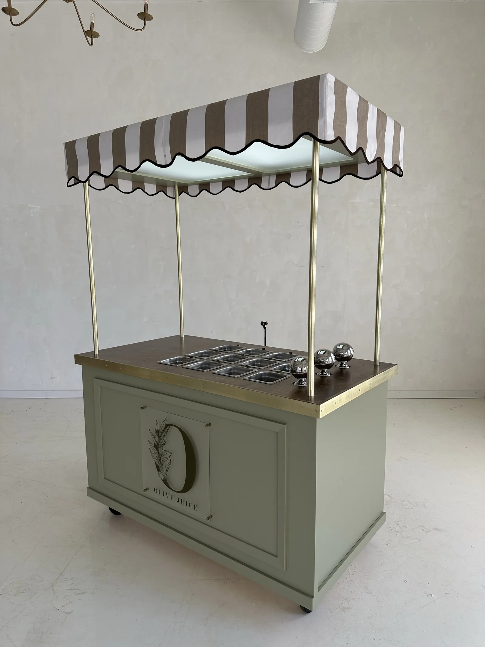 A sage green RidgeCraft awning cart with brass posts, a striped scalloped canopy and a wood top set with stainless wells