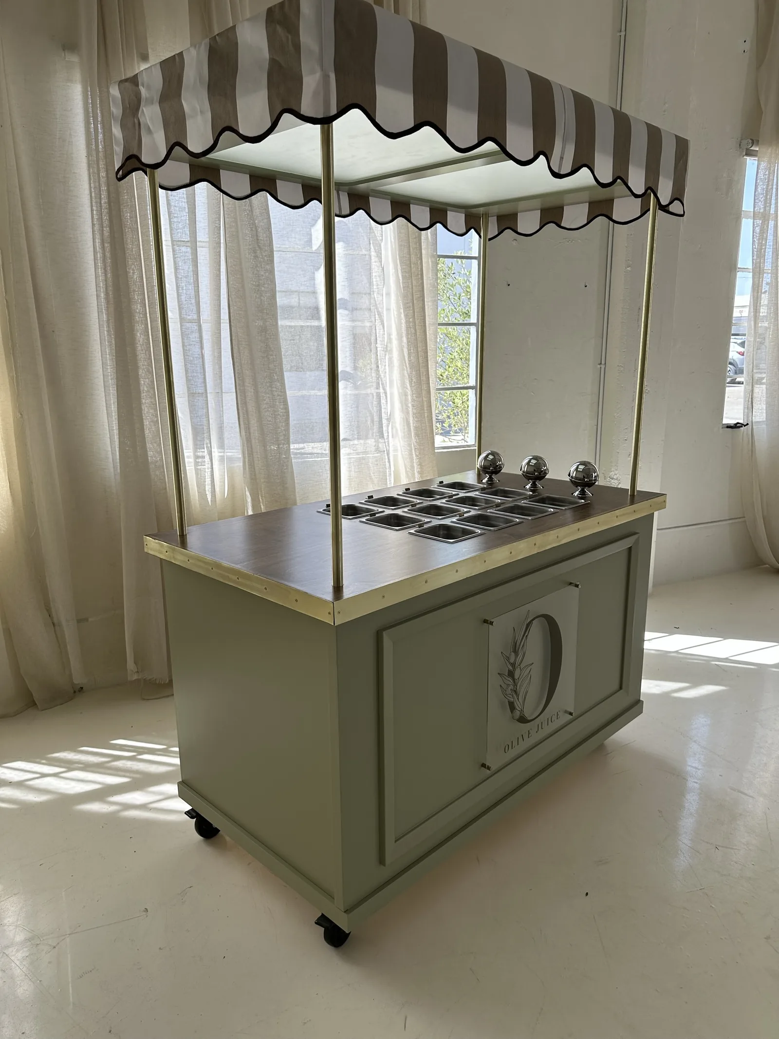 A fluted-front cart with a striped awning canopy and brass posts, indoors by a curtained window
