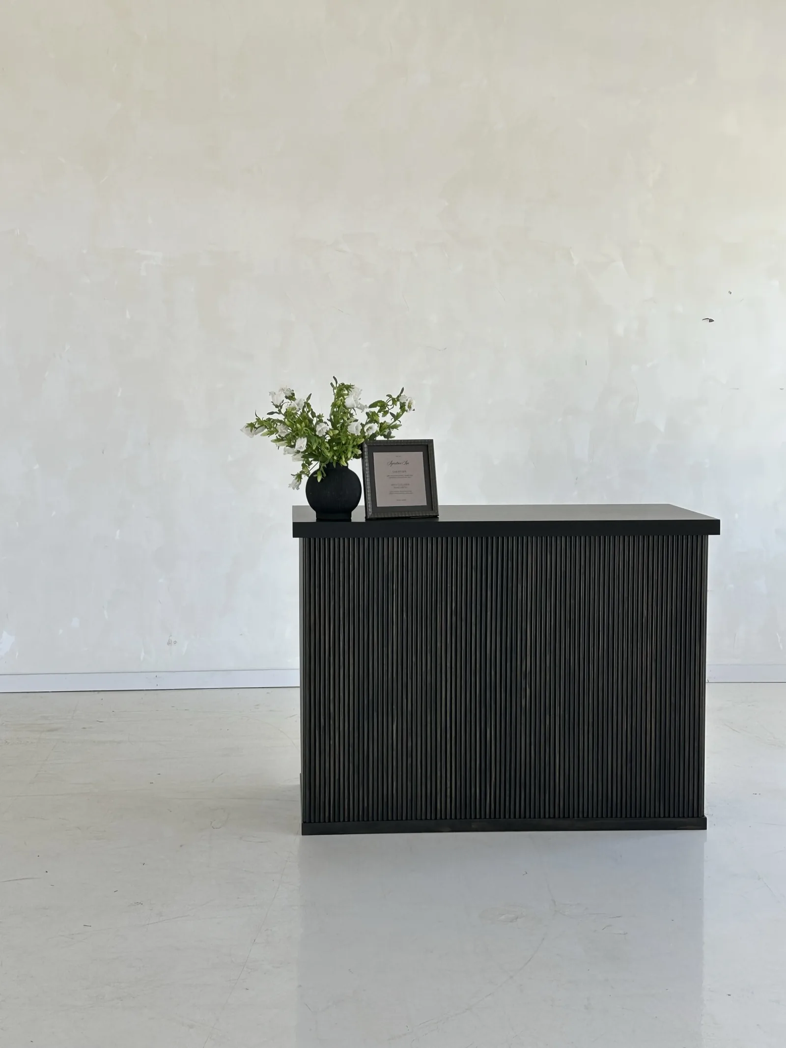 A RidgeCraft bar with a fluted front painted black, styled with a vase and a framed print
