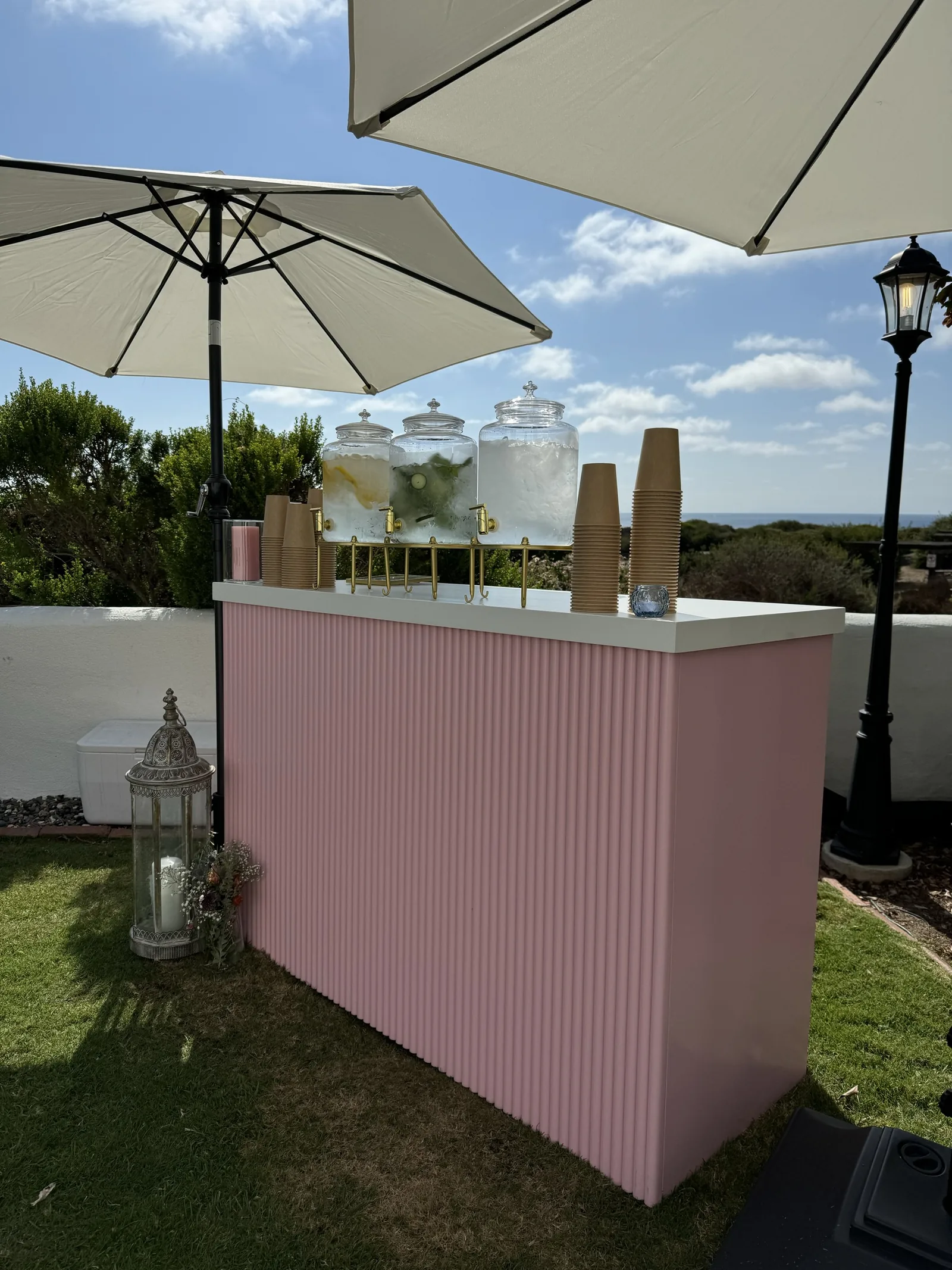A pink corrugated-front bar set up on a coastal patio with drink dispensers on top
