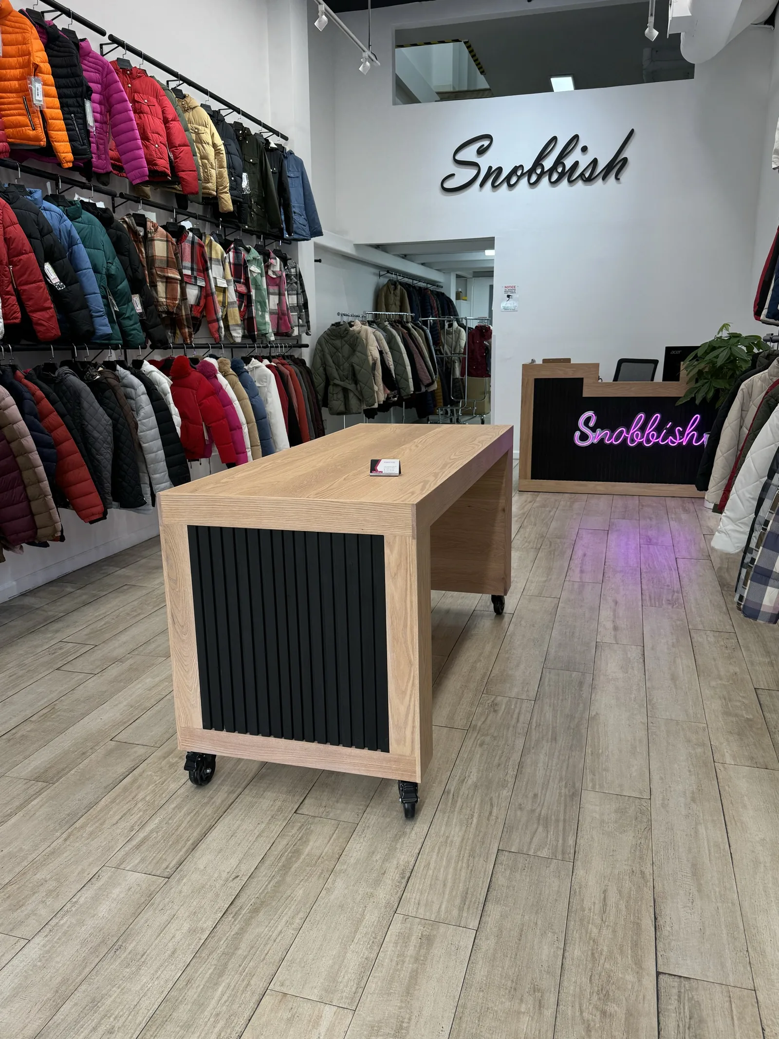 A wood-topped RidgeCraft counter on the floor of a clothing shop beside a neon sign